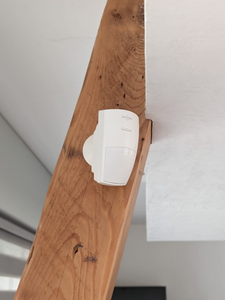 Détecteur de mouvement volumétrique Daitem installé sur une poutre en bois par JOUVE SCF, pour la sécurisation intérieure d’un bâtiment contre les intrusions.
