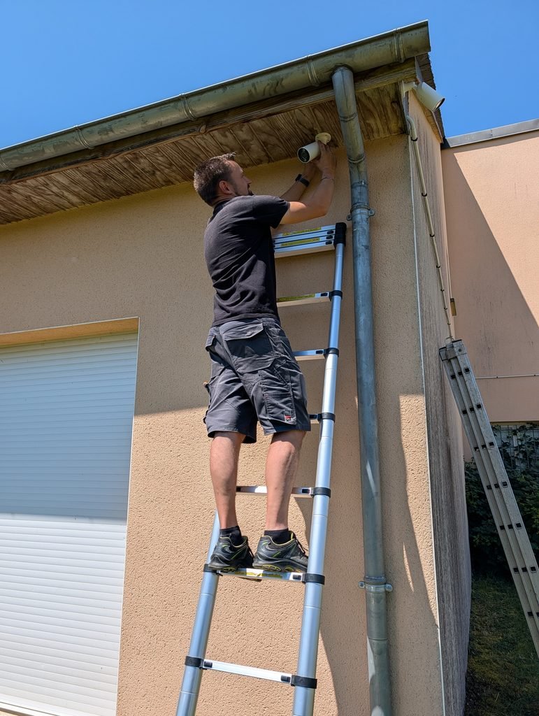 Vente et installation d'une caméra de vidéosurveillance extérieure sous une avancée de toiture, réalisée par JOUVE SCF pour sécuriser un bâtiment.
